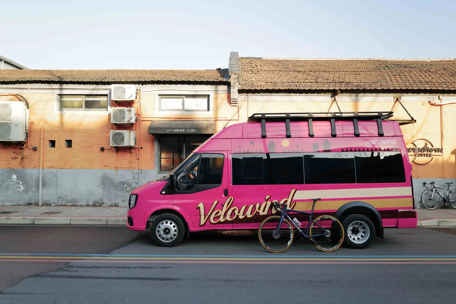 粉色 Velowind 户外运动专用车与公路自行车停在城市街道旁。